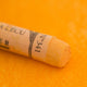 A close-up of a yellow Sennelier extra soft pastel. on the same coloured background, with the colour information printed on the paper wrap.