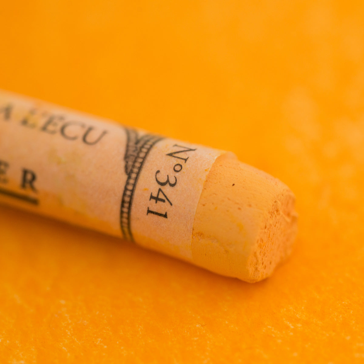 A close-up of a yellow Sennelier extra soft pastel. on the same coloured background, with the colour information printed on the paper wrap.