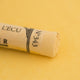 A close-up of a yellow Sennelier extra soft pastel. on the same coloured background, with the colour information printed on the paper wrap.