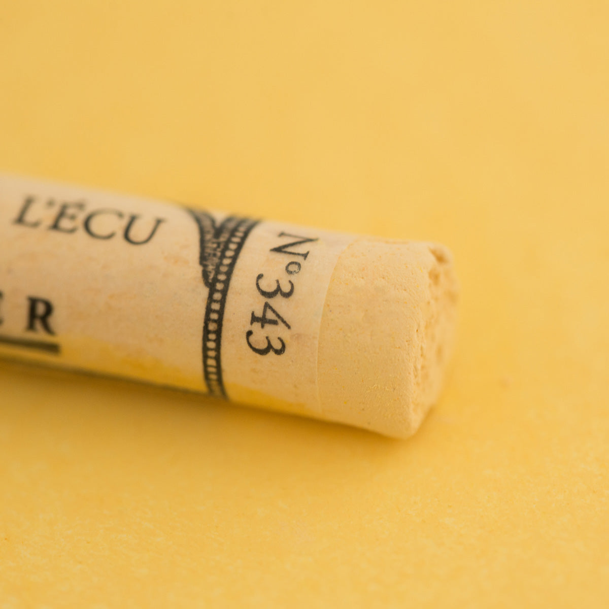 A close-up of a yellow Sennelier extra soft pastel. on the same coloured background, with the colour information printed on the paper wrap.