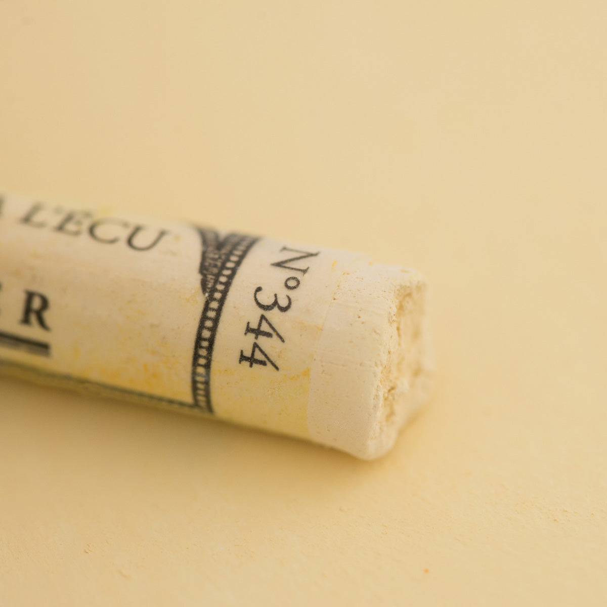 A close-up of a pale yellow Sennelier extra soft pastel. on the same coloured background, with the colour information printed on the paper wrap.