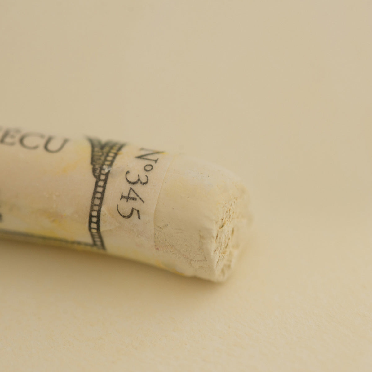 A close-up of a pale yellow Sennelier extra soft pastel. on the same coloured background, with the colour information printed on the paper wrap.