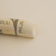 A close-up of a white Sennelier extra soft pastel. on the same coloured background, with the colour information printed on the paper wrap.