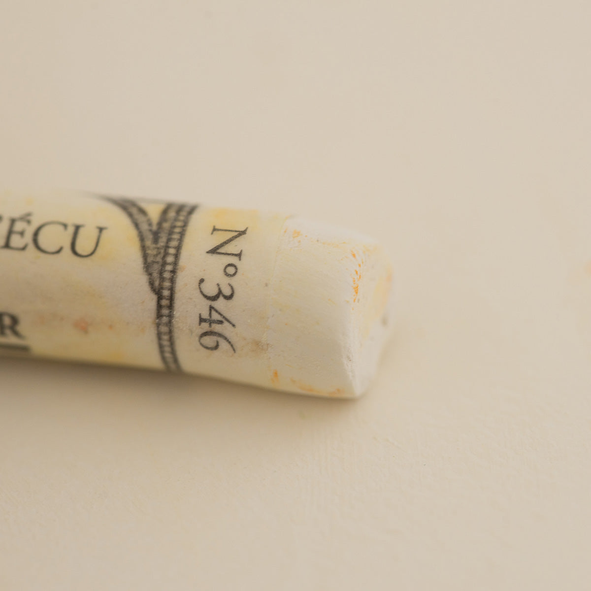 A close-up of a white Sennelier extra soft pastel. on the same coloured background, with the colour information printed on the paper wrap.