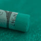 A close-up of a green Sennelier extra soft pastel. on the same coloured background, with the colour information printed on the paper wrap.