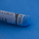 A close-up of a blue Sennelier extra soft pastel on the same coloured background, with the colour information printed on the paper wrap.