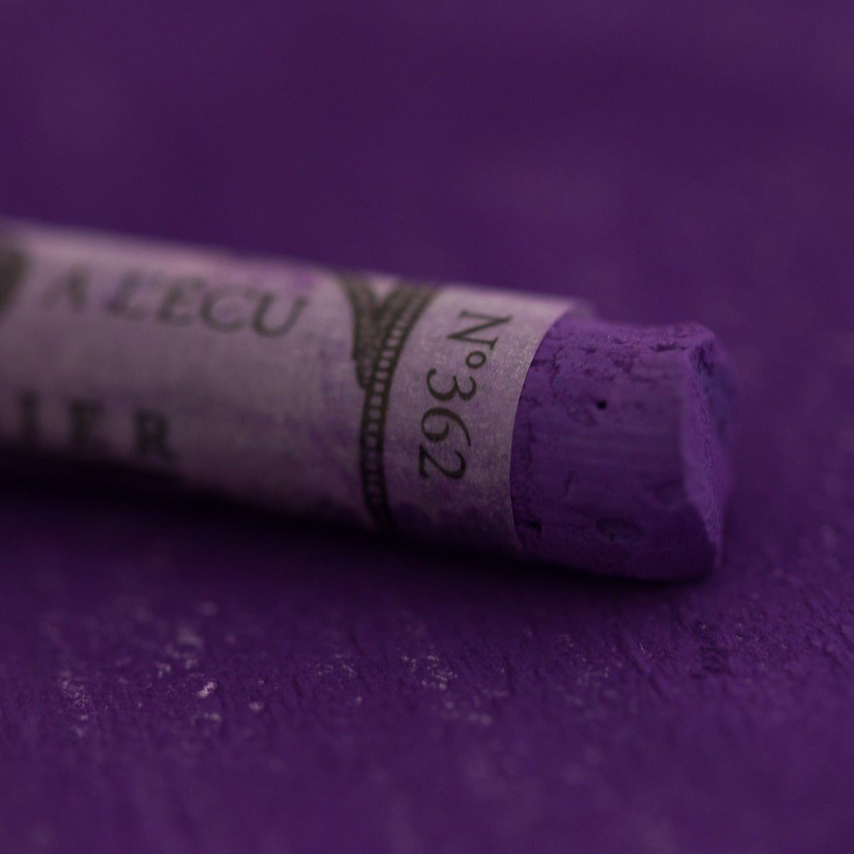  A close-up of a purple Sennelier extra soft pastel on the same coloured background, with the colour information printed on the paper wrap.