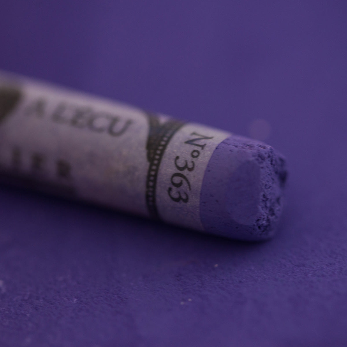  A close-up of a purple Sennelier extra soft pastel on the same coloured background, with the colour information printed on the paper wrap.
