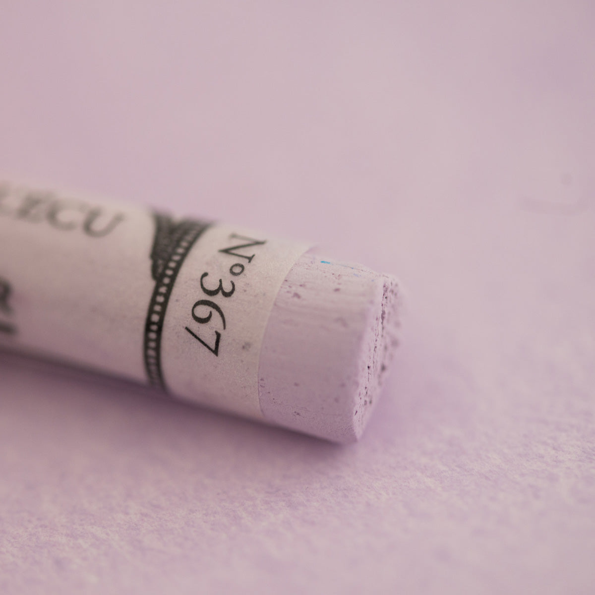  A close-up of a pale purple Sennelier extra soft pastel on the same coloured background, with the colour information printed on the paper wrap.