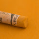 A close-up of a deep yellow Sennelier extra soft pastel. on the same coloured background, with the colour information printed on the paper wrap.
