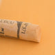 A close-up of a light yellow Sennelier extra soft pastel. on the same coloured background, with the colour information printed on the paper wrap.