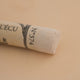 A close-up of a white Sennelier extra soft pastel. on the same coloured background, with the colour information printed on the paper wrap.