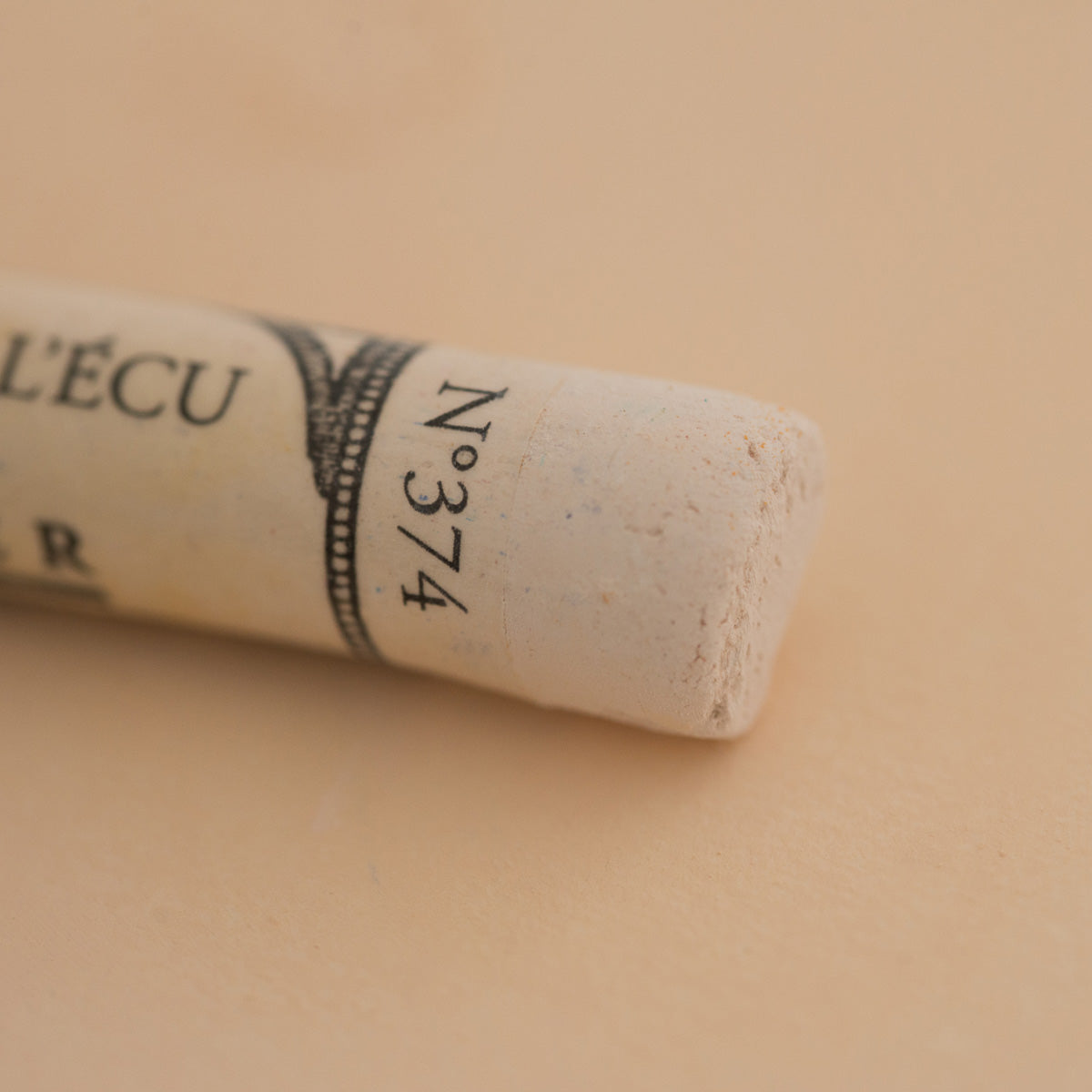 A close-up of a white Sennelier extra soft pastel. on the same coloured background, with the colour information printed on the paper wrap.