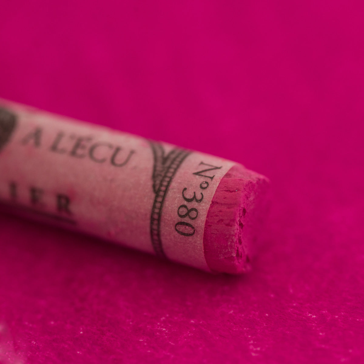 A close-up of a red Sennelier extra soft pastel. on the same coloured background, with the colour information printed on the paper wrap.