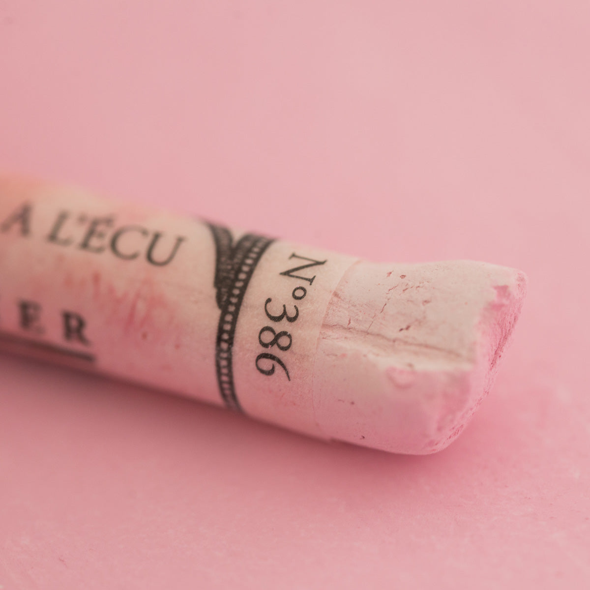 A close-up of a light pink Sennelier extra soft pastel. on the same coloured background, with the colour information printed on the paper wrap.