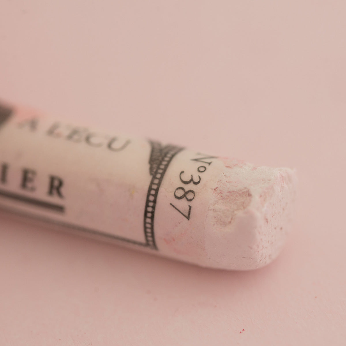 A close-up of a white Sennelier extra soft pastel. on the same coloured background, with the colour information printed on the paper wrap.