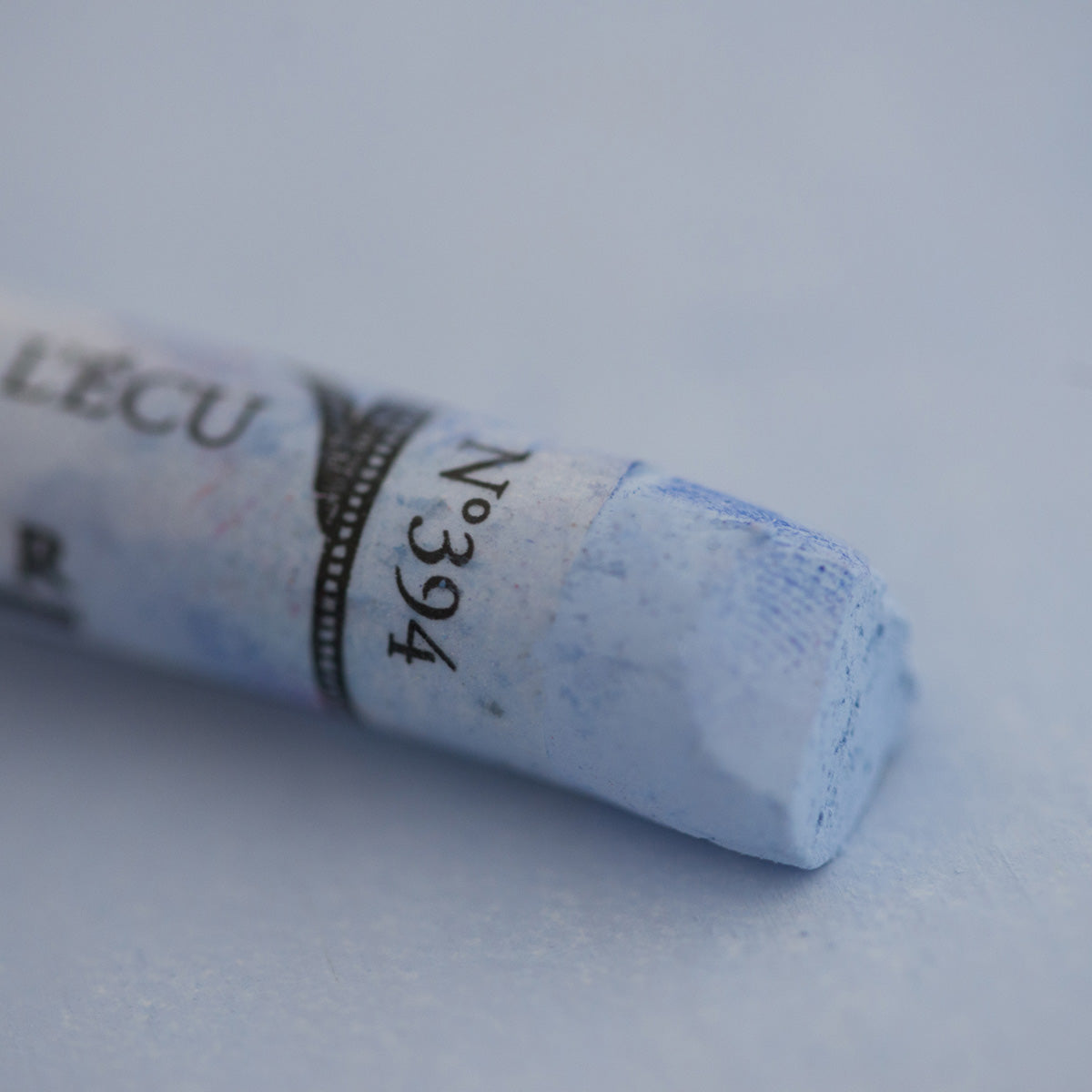 A close-up of a pale blue Sennelier extra soft pastel on the same coloured background, with the colour information printed on the paper wrap.