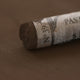 A close-up of a dark brown Sennelier extra soft pastel. on the same coloured background, with the colour information printed on the paper wrap.