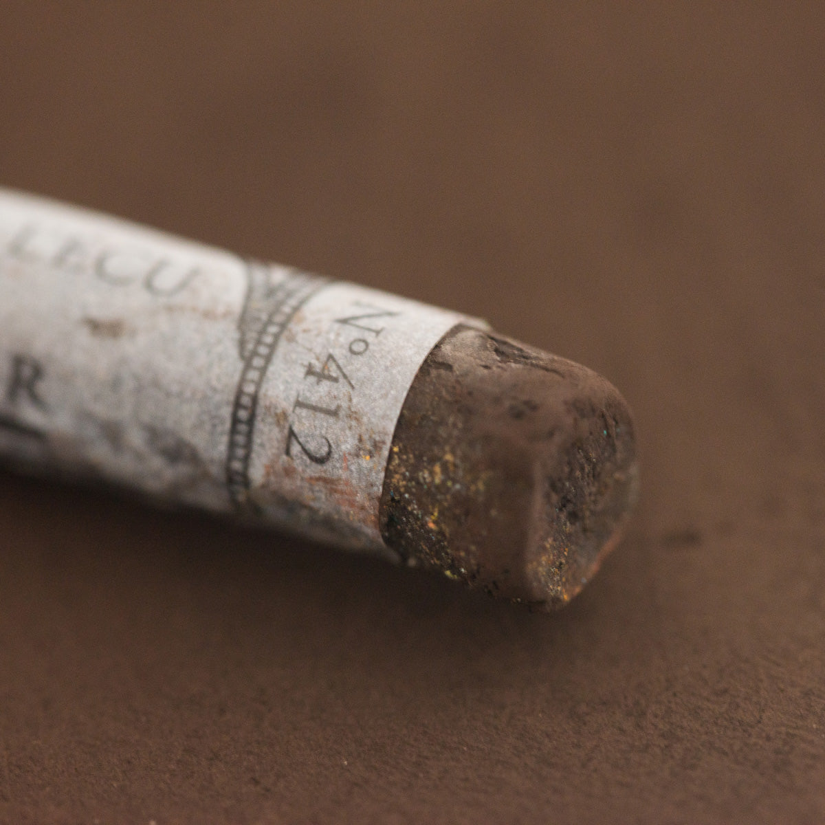 A close-up of a brown Sennelier extra soft pastel with the colour information printed on the paper wrap.