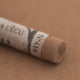 A close-up of a brown Sennelier extra soft pastel with the colour information printed on the paper wrap.