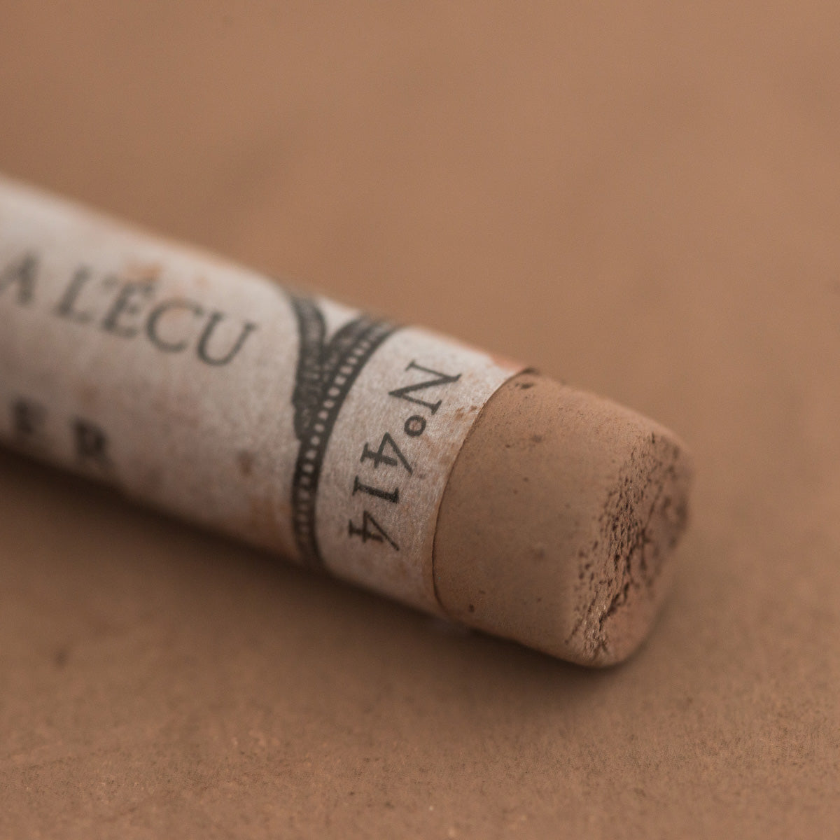 A close-up of a brown Sennelier extra soft pastel with the colour information printed on the paper wrap.
