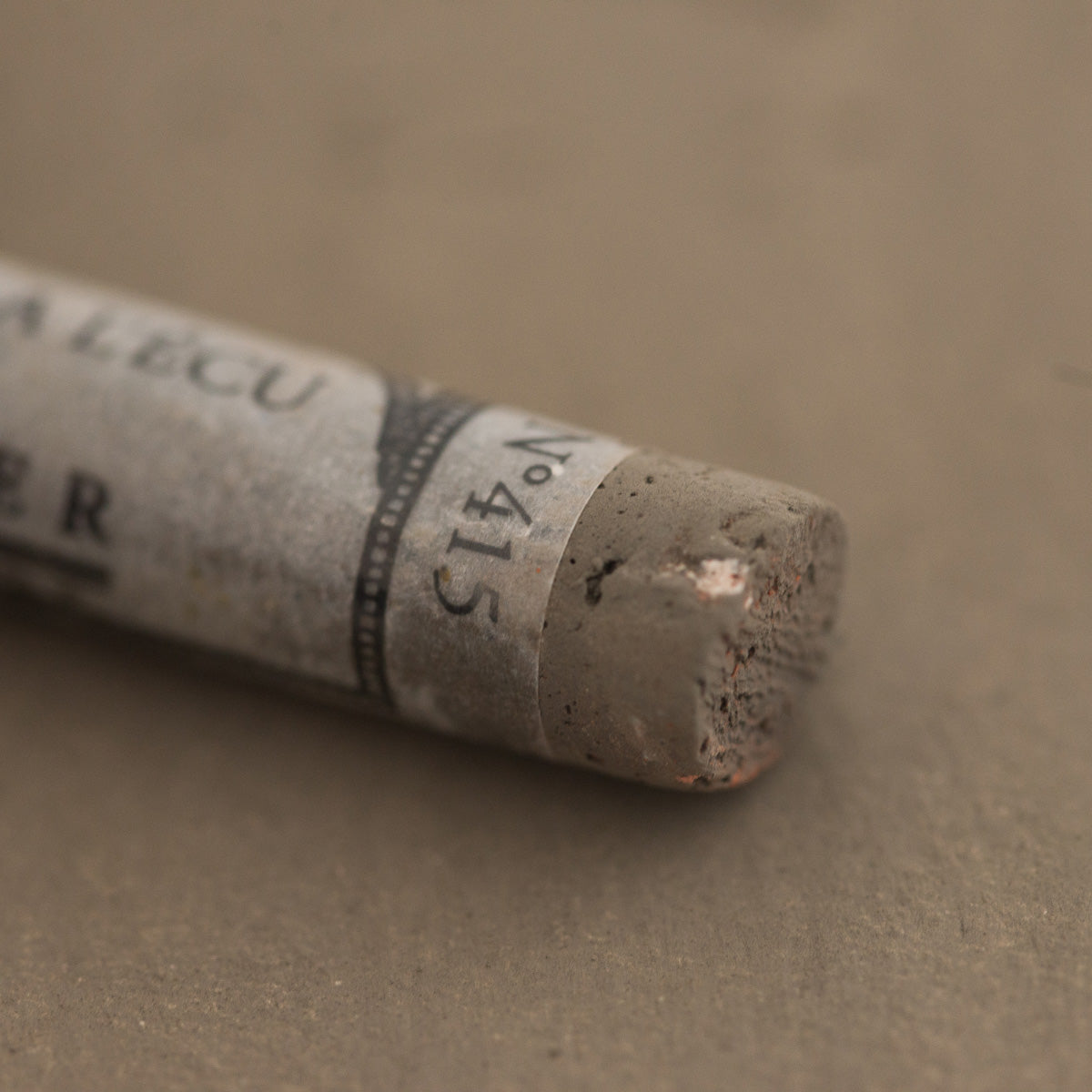 A close-up of a brown Sennelier extra soft pastel with the colour information printed on the paper wrap.