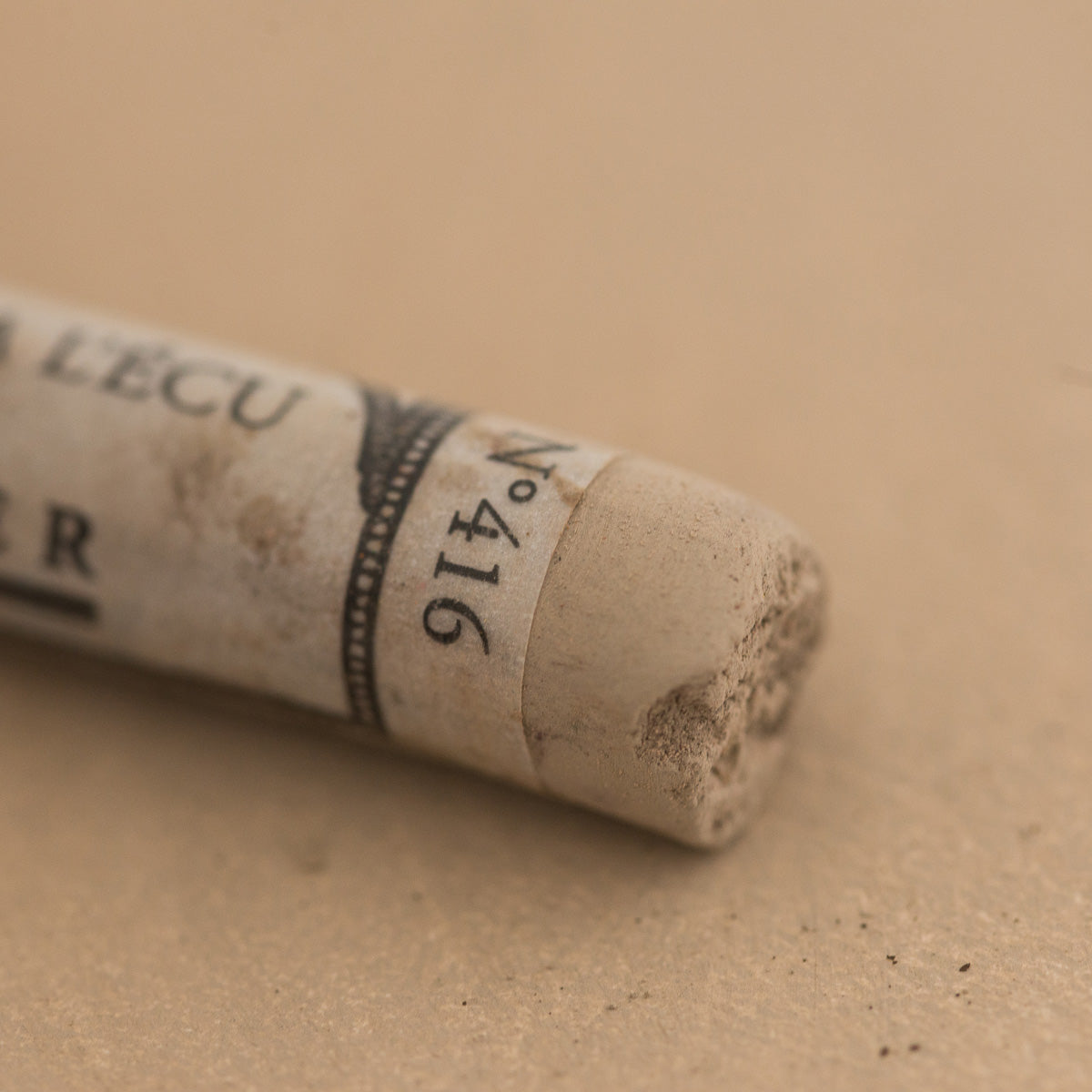 A close-up of a brown Sennelier extra soft pastel with the colour information printed on the paper wrap.