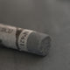 A close-up of a dark grey Sennelier extra soft pastel. on the same coloured background, with the colour information printed on the paper wrap.