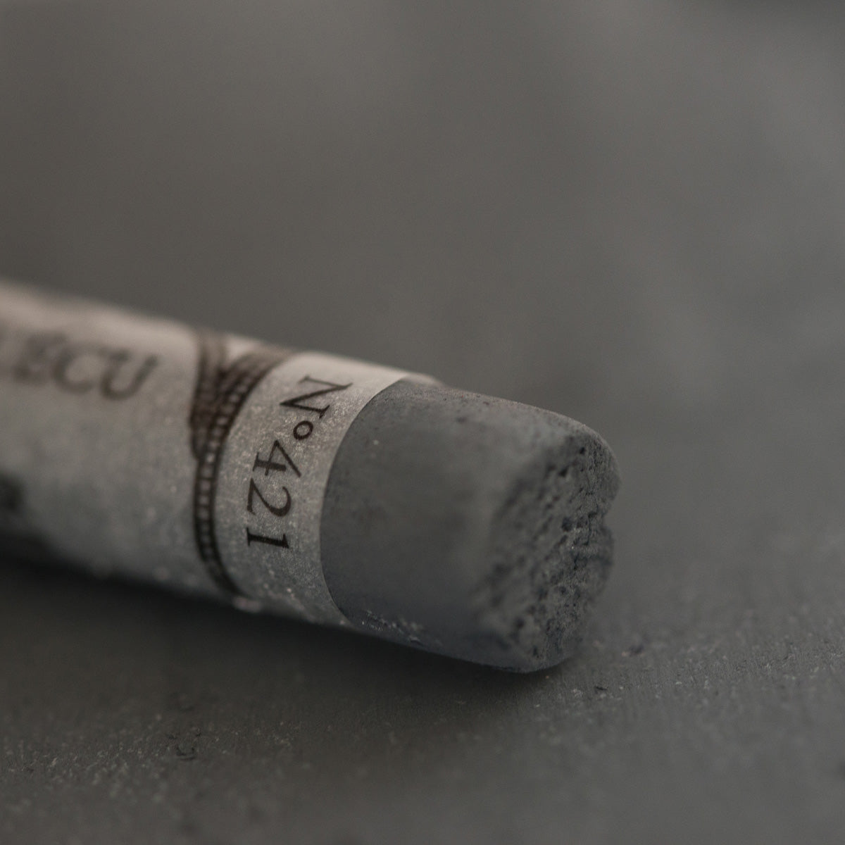 A close-up of a dark grey Sennelier extra soft pastel. on the same coloured background, with the colour information printed on the paper wrap.