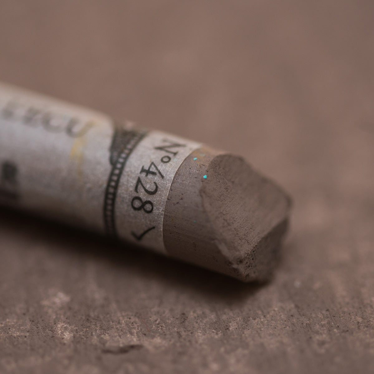 A close-up of a brown Sennelier extra soft pastel. on the same coloured background, with the colour information printed on the paper wrap.