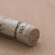 A close-up of a light brown Sennelier extra soft pastel. on the same coloured background, with the colour information printed on the paper wrap.
