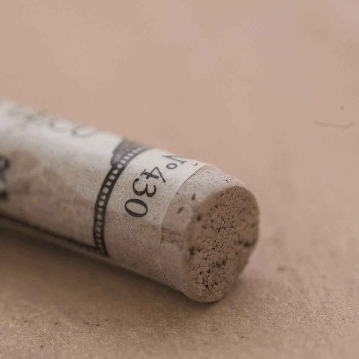 A close-up of a light brown Sennelier extra soft pastel. on the same coloured background, with the colour information printed on the paper wrap.