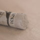A close-up of a light brown Sennelier extra soft pastel. on the same coloured background, with the colour information printed on the paper wrap.