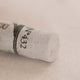 A close-up of a white Sennelier extra soft pastel. on the same coloured background, with the colour information printed on the paper wrap.