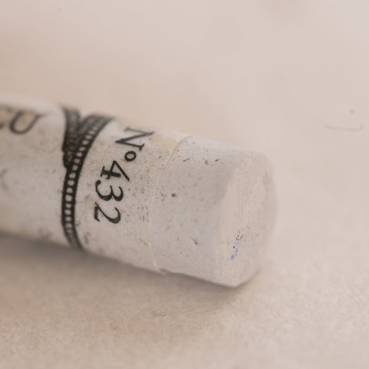 A close-up of a white Sennelier extra soft pastel. on the same coloured background, with the colour information printed on the paper wrap.