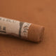 A close-up of a Sennelier extra soft pastel on a brown background with the colour information printed on the paper wrap.