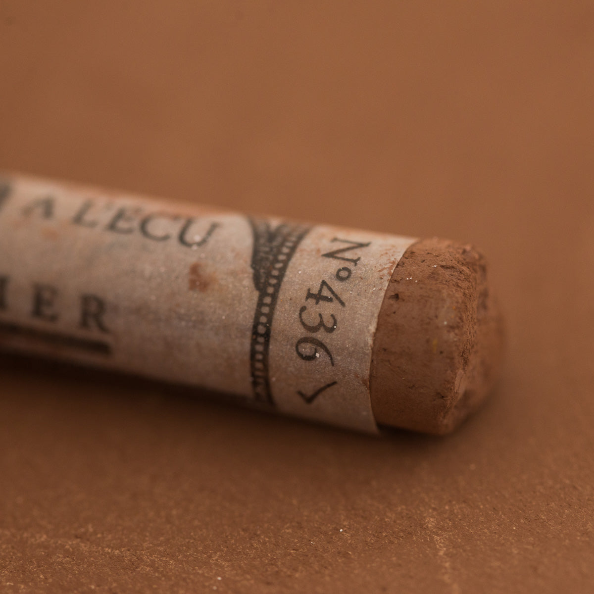 A close-up of a Sennelier extra soft pastel on a brown background with the colour information printed on the paper wrap.