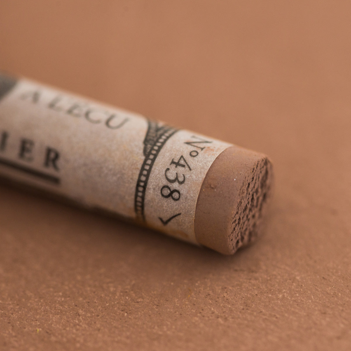A close-up of a Sennelier extra soft pastel on a brown background with the colour information printed on the paper wrap.