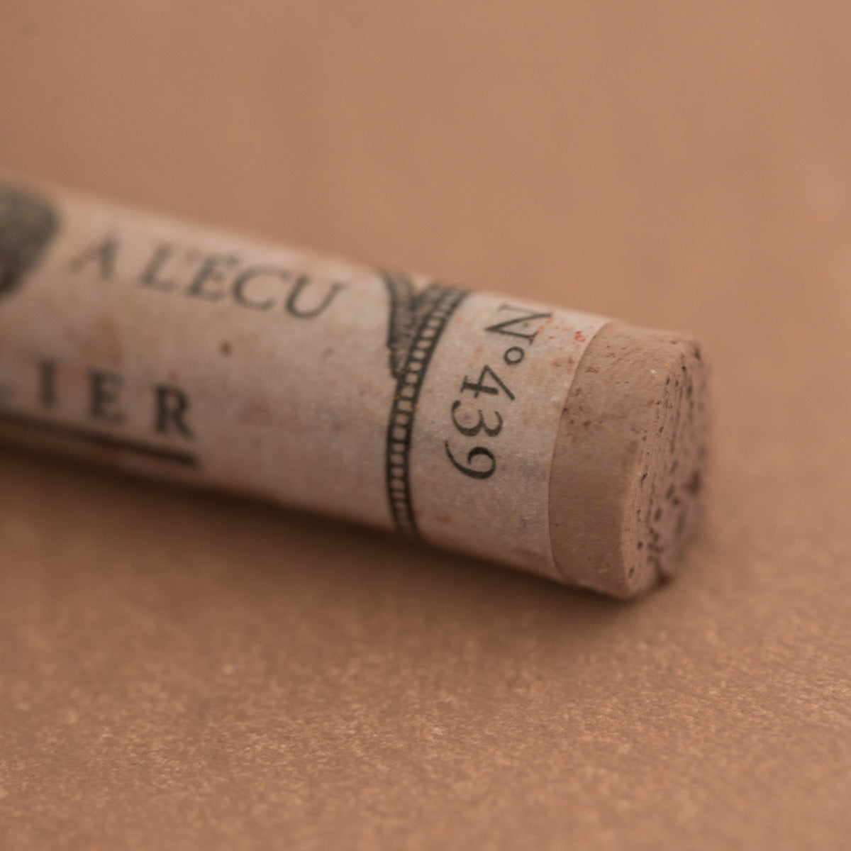 A close-up of a Sennelier extra soft pastel on a brown background with the colour information printed on the paper wrap.