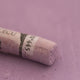 A close-up of a purple Sennelier extra soft pastel with the colour information printed on the paper wrap.