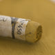 A close-up of a brown Sennelier extra soft pastel. on the same coloured background, with the colour information printed on the paper wrap.