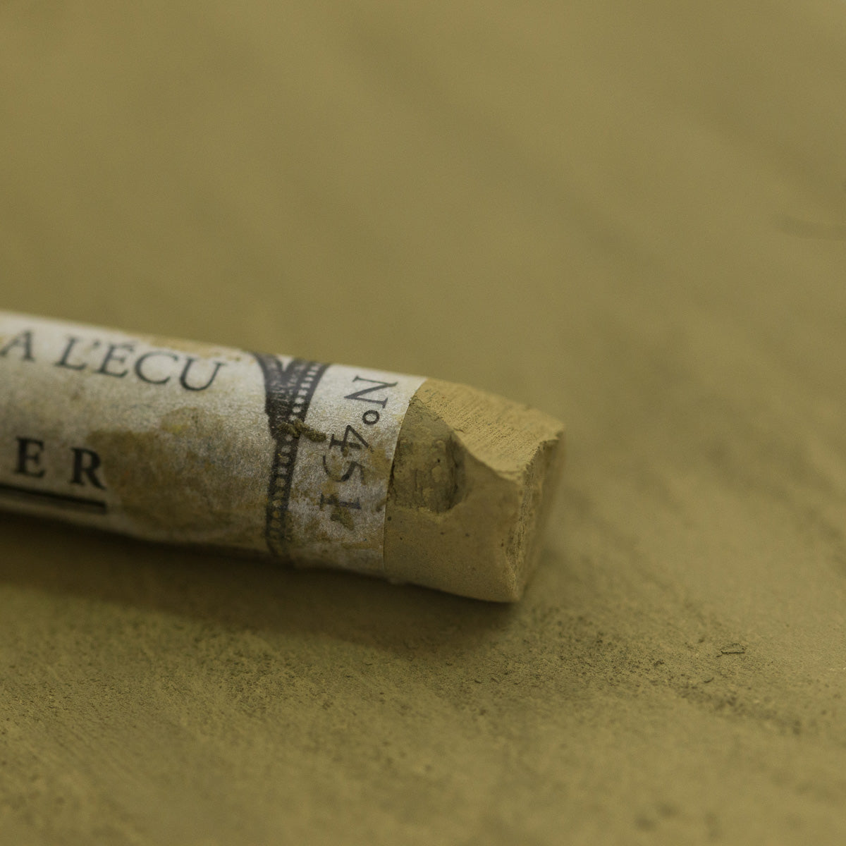 A close-up of a brown Sennelier extra soft pastel. on the same coloured background, with the colour information printed on the paper wrap.