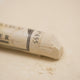 A close-up of a white Sennelier extra soft pastel. on the same coloured background, with the colour information printed on the paper wrap.