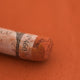 A close-up of a dusty red Sennelier extra soft pastel with the colour information printed on the paper wrap.