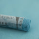 A close-up of a blue Sennelier extra soft pastel on the same coloured background, with the colour information printed on the paper wrap.
