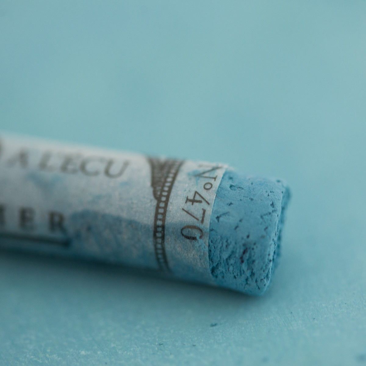 A close-up of a blue Sennelier extra soft pastel on the same coloured background, with the colour information printed on the paper wrap.
