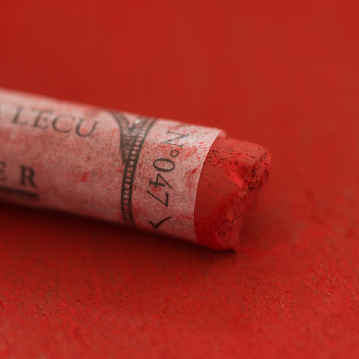 A close-up of a red Sennelier extra soft pastel with the colour information printed on the paper wrap.