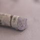 A close-up of a grey Sennelier extra soft pastel. on the same coloured background, with the colour information printed on the paper wrap.