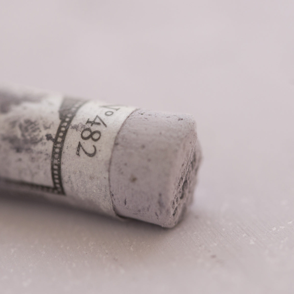 A close-up of a grey Sennelier extra soft pastel. on the same coloured background, with the colour information printed on the paper wrap.