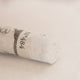 A close-up of a white Sennelier extra soft pastel. on the same coloured background, with the colour information printed on the paper wrap.